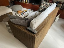 divano in rattan di colore marrone a tre posti con cuscini bianchi 