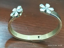 BRACCIALE RIGIDO IN METALLO DORATO CON FIORI IN STRASS ALLE ESTREMITÀ, FIRMATO.