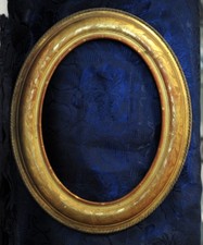 Coppia di cornici ovali in legno inciso a motivi floreali e dorate a foglia