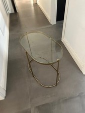 Tavolino moderno con struttura dorata e piano in vetro.