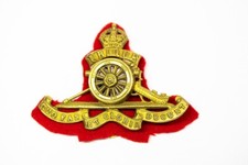 ROYAL ARTILLERY BRITISH MILITARY CAP BADGE WITH RED FELT BACK AND MOVING WHEEL.